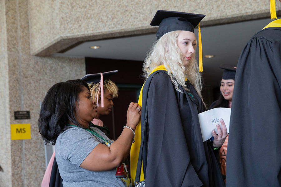 An almost grad gets a little help adjusting her regalia
