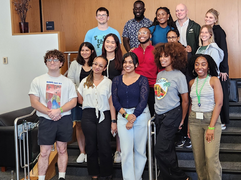 A group of sixteen people smiling and posing together on an indoor staircase.