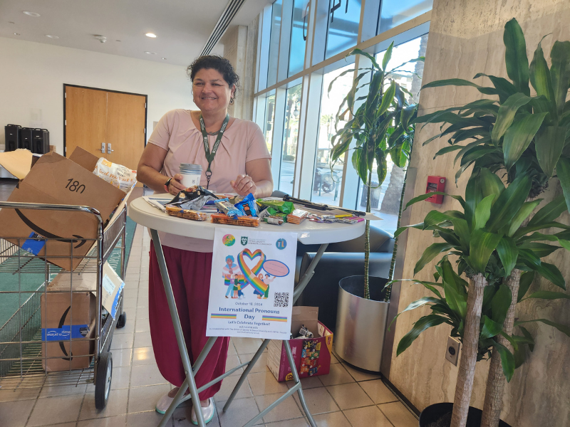 Woman smiling behind a table with snacks in a bright room with large plants.