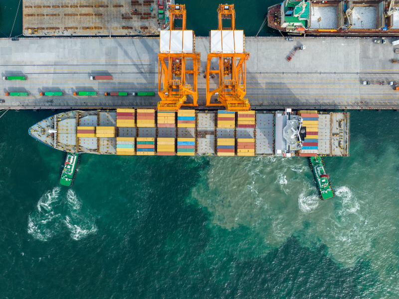 A Cargo ship docked at port, seen from directly above, in bright water.