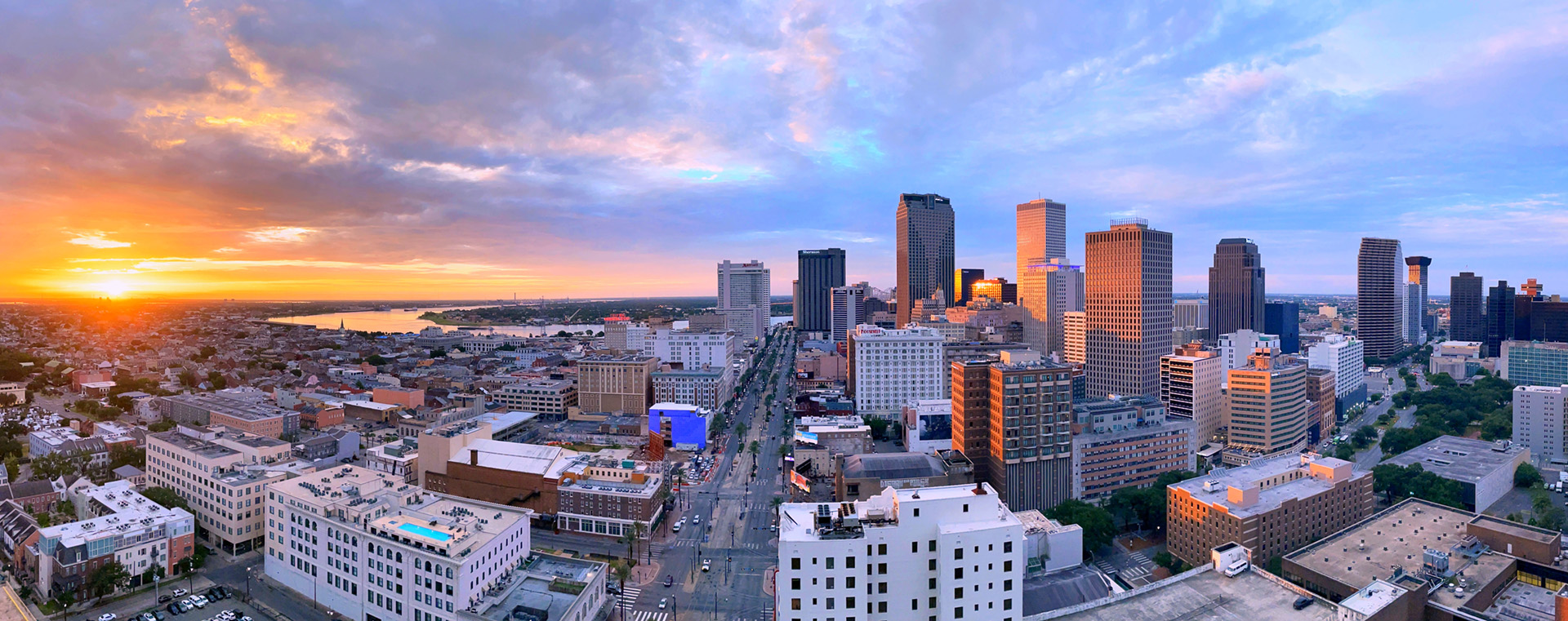 Panoramic New Orleans skyline at sunset, golden light on buildings, blue sky, distant water