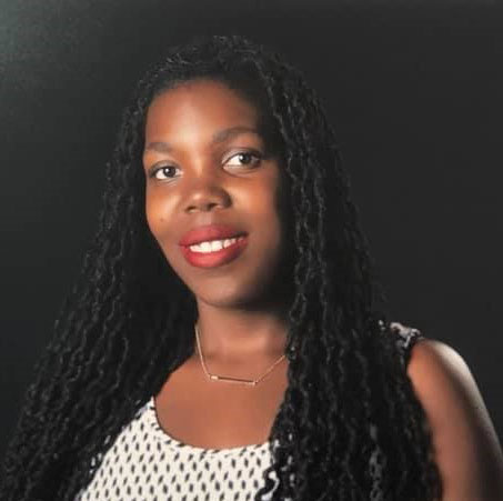 Smiling Black woman with long braids, red lipstick, and a patterned top.