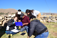 Five students gather outdoors, working collectively, hills in background.