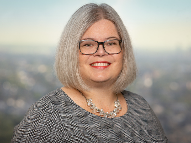 Headshot of Dr. Christine Arcari, wearing a patterned top, city background.