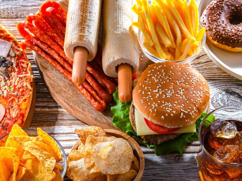 Assortment of fast food: pizza, hot dogs, fries, burger, chips, donut, soda.