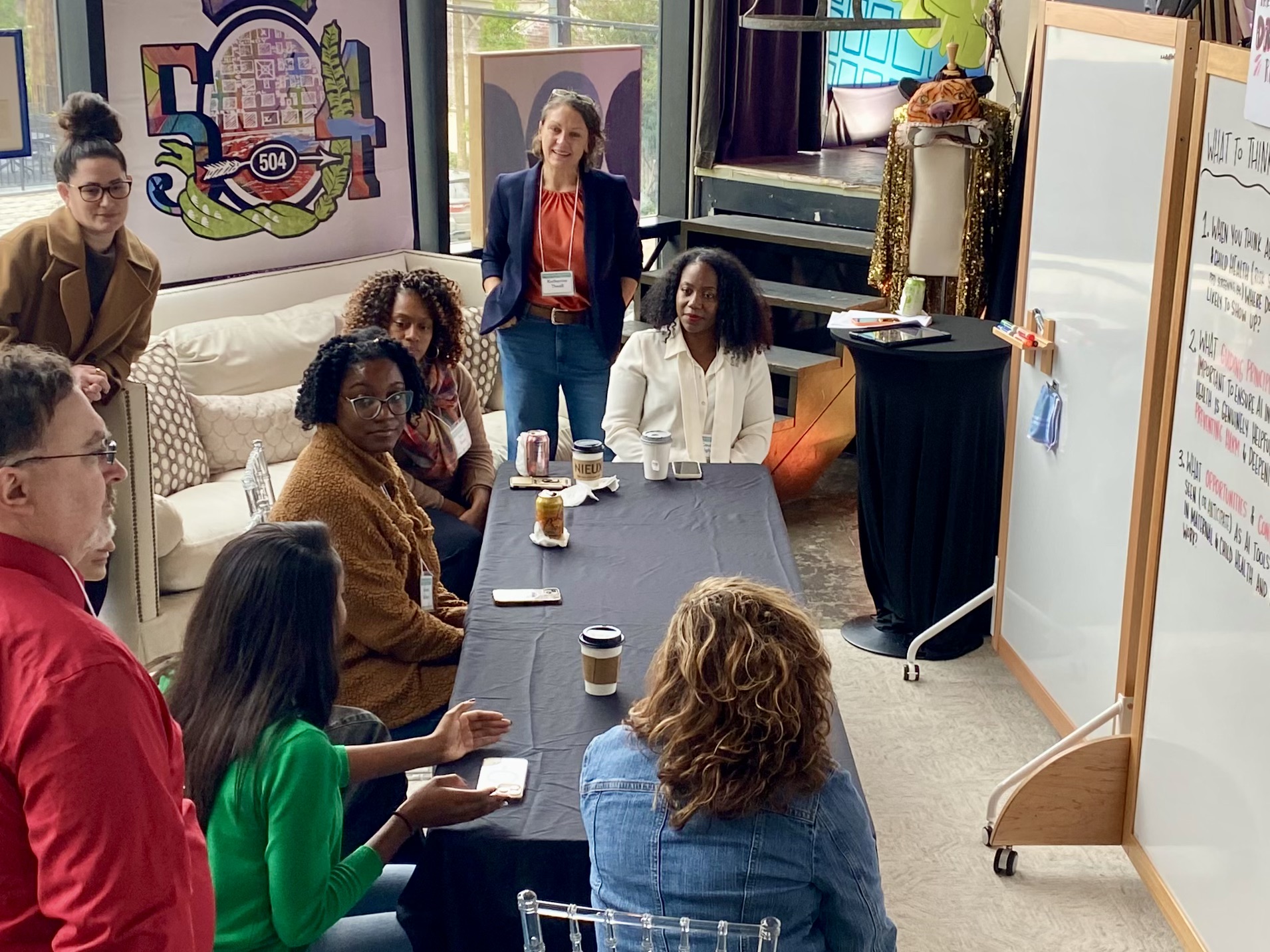 Diverse group of people in a meeting room with a whiteboard and colorful mural.