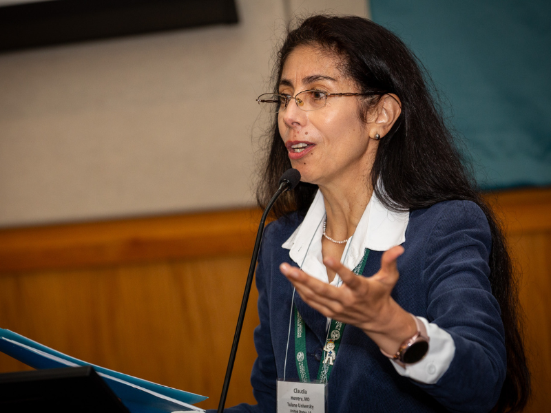 Claudia Herrera speaks at a lectern, gesturing with her hand.