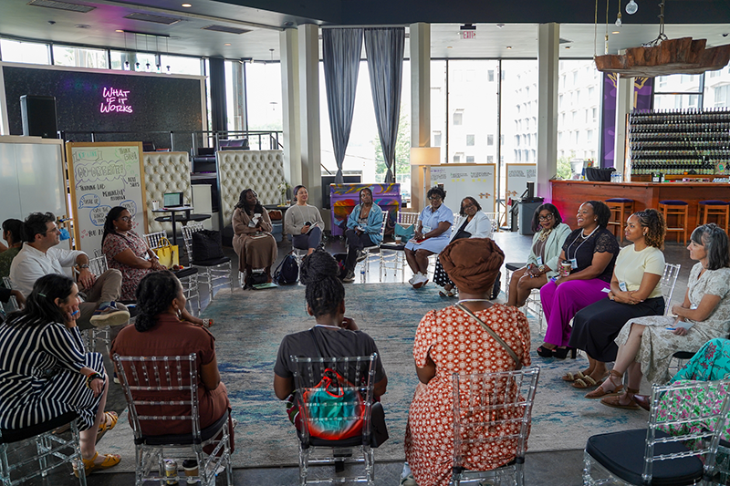 Attendees seated in a circle, engaged in discussion at a bright event space.