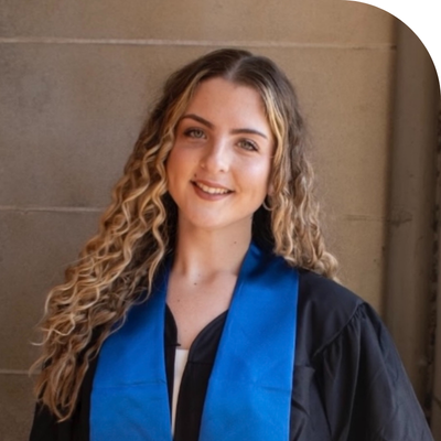 Smiling young woman in black graduation gown with blue stole and curly hair.