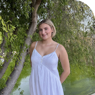 A white young lady in a white summer dress standing in park next to a tree