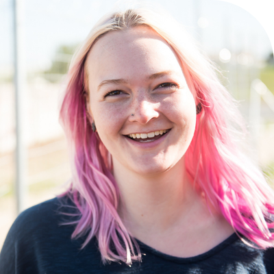 Smiling young woman with bright pink and blonde hair, outdoors.