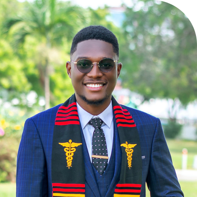 Young Black man in suit and graduation stole with caduceus, smiling outdoors.