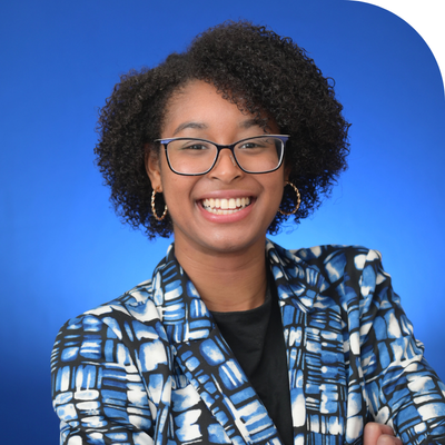 black young lady smiling with glasses and curly black hair in a blue multi colored jacket and black inner top