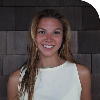 Smiling young woman with long hair and a turquoise necklace against a wooden wall.