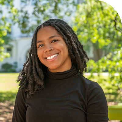 Smiling young Black woman with dreadlocks in a black top outdoors.