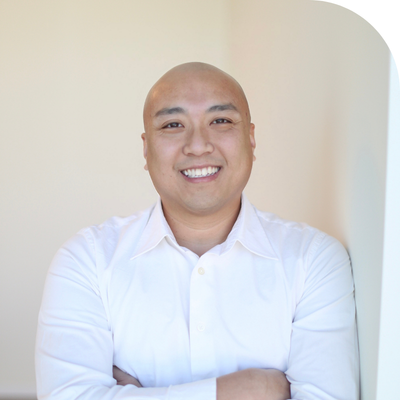 Photograph of a smiling bald Asian man, wearing a white shirt with crossed arms.