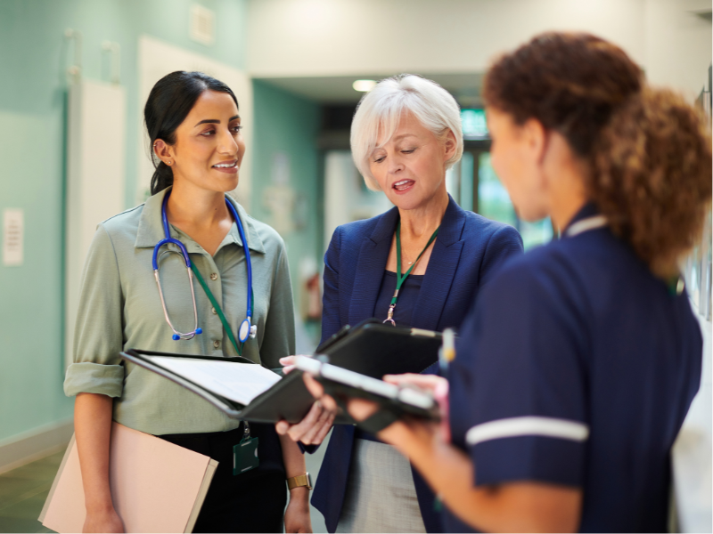 Photograph of three diverse medical professionals collaborating in a hospital corridor.
