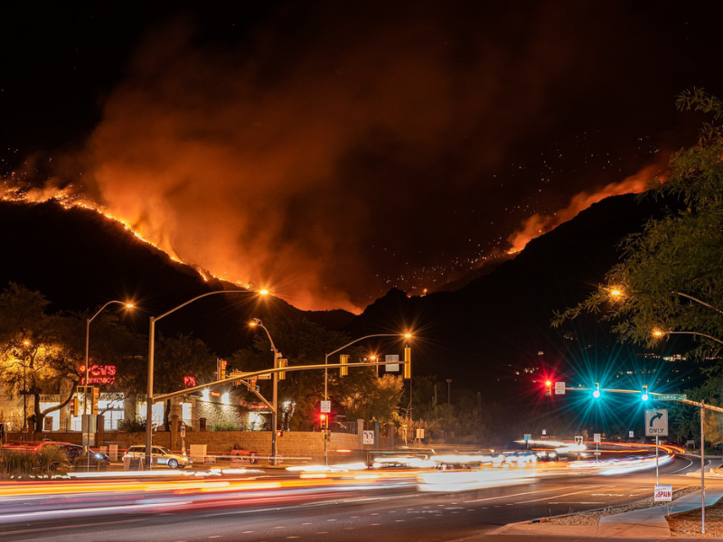 Photograph of a hillside engulfed in a wildfire at night with traffic light trails.