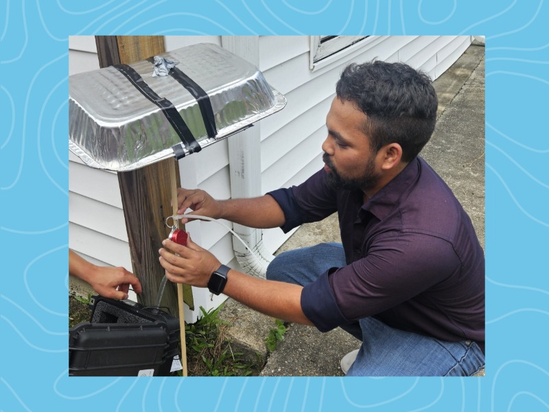 Photograph of a man in a dark shirt installing a device on a wooden post outdoors.