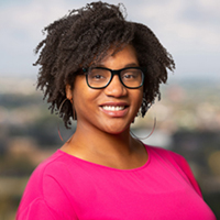 Caryn Bell, wearing a pink shirt, smiling, Assistant Professor, Social, Behavioral & Population Sciences