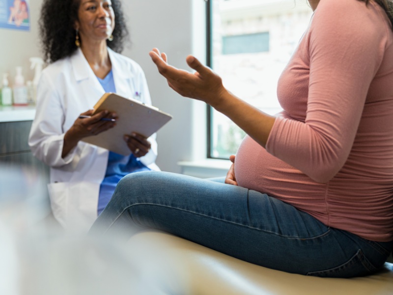 Pregnant woman in pink shirt and jeans faces her doctor with her hand gesturing