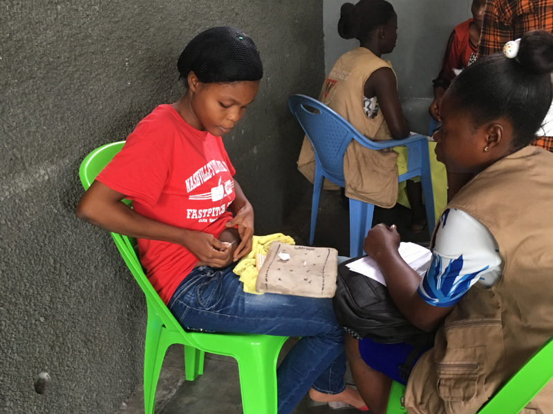 Child administering a shot to himself while a healthcare worker looks on