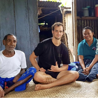 Alex Widman, sitting cross legged with two Peace Corps hosts