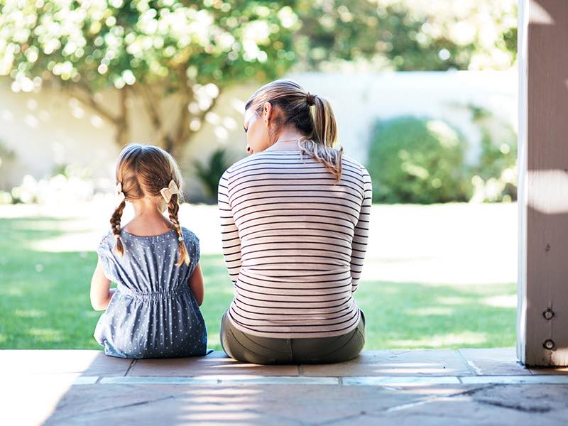 Photo of a mother and daughter sitting on a porch, having a discussion.