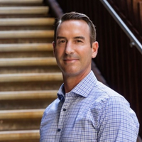 Greg Collins, headshot, standing in front of stairs