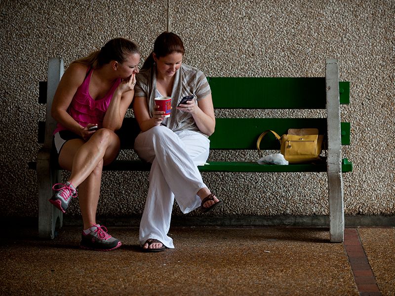 two girls on a bench looking concerned with cell phone