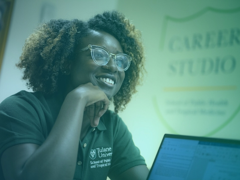 African-American woman wearing glasses looking studious sitting at a desk, career studio signage in background