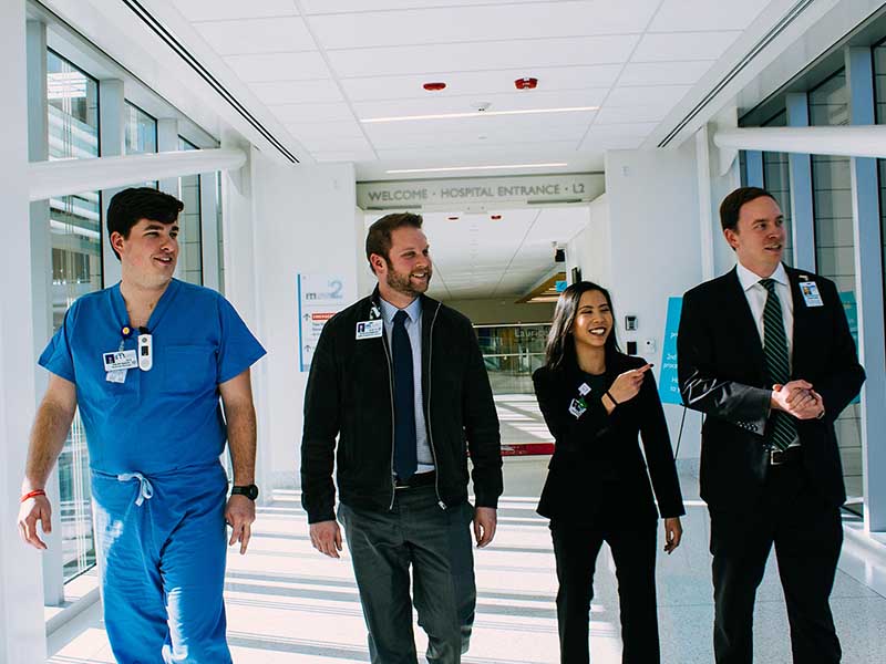 three men and one woman alumni walking in children's hospital, one in scrubs