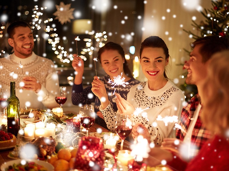 Family sitting down at a dining table celebrating the holidays in festive sweaters, while holding sparklers