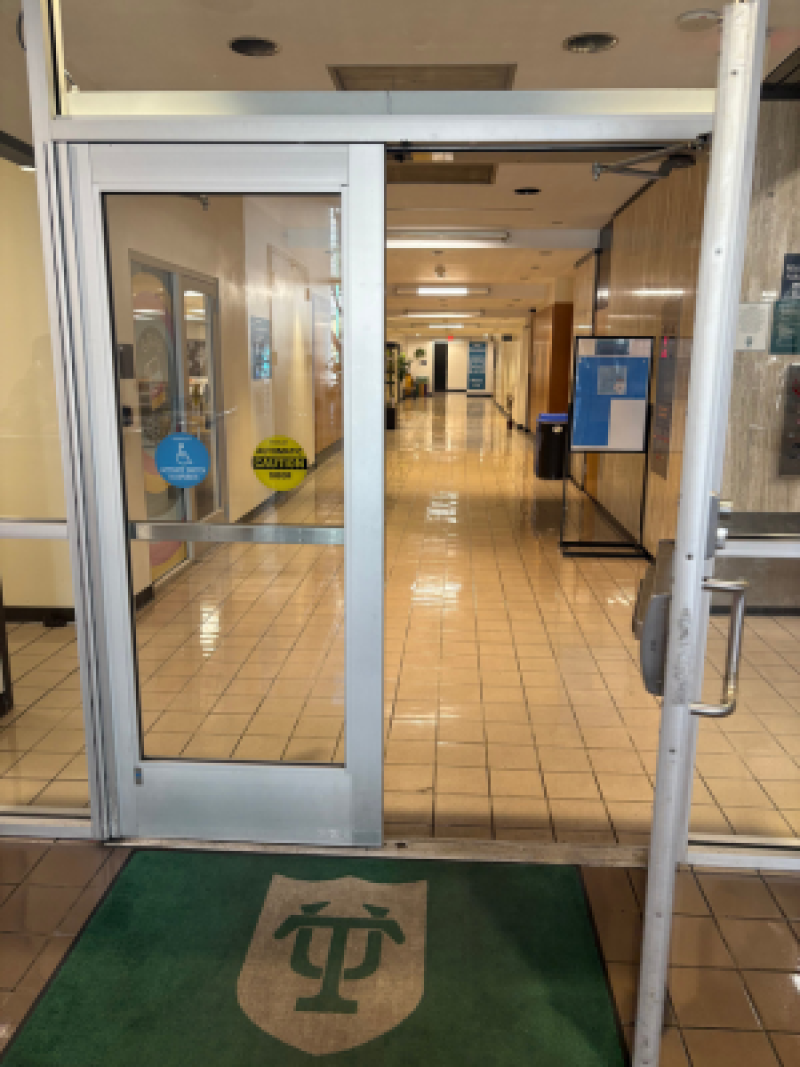 Glass entrance door leading to first floor hallway in Tidewater tiled hallway with a green Tulane University logo mat.