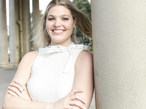 Kaylin Swoboda leaning against a column, smiling, arms crossed