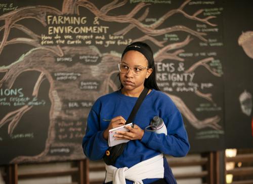 Student at Grow Dat Youth Farm in front of illustration that reads "farming & environment"