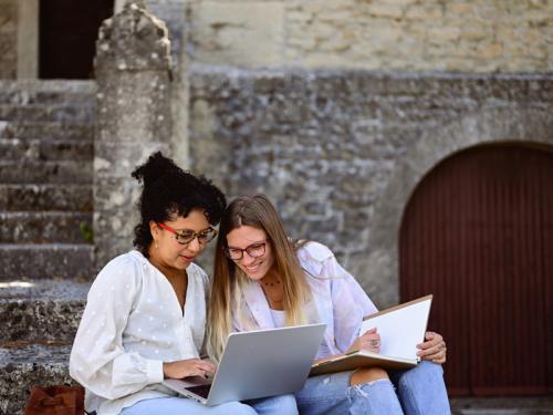 Transforming Public Health with AI in the Celia Scott Weatherhead School of Public Health and Tropical Medicine Two female students looking at laptops outside of a university building