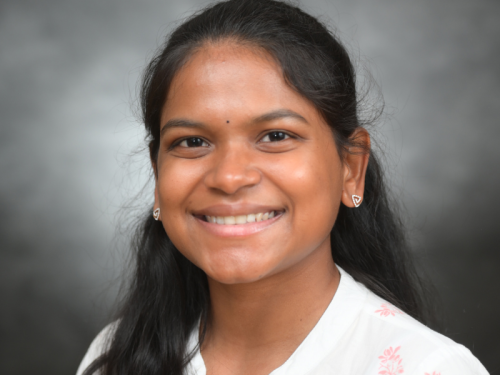 Harini Durai, headshot, smiling and looking directly into camera, wearing a white blouse with tiny pink flowers. 
