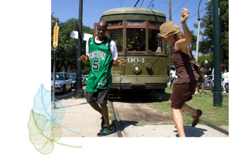 Man in green jersey and woman in brown dress dancing on street, old green tram behind.