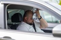 Man holding a water bottle to his forehead to cool off in his car