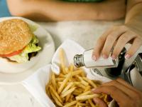 High-salt diet may raise cardiovascular disease risk for kidney disease patients a hand shown shaking salt on to french fires with burger in background