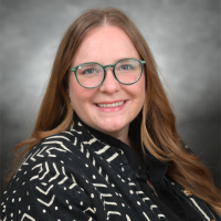 Casey Douma | Global Scholars Program Casey Douma headshot, wearing a black top with white, pattern, smiling at camera, wearing glasses