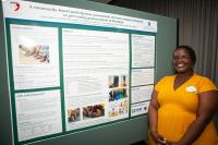 Gloria Igihozo stands next to her first place poster in the 2025 Delta Omega poster comeptition