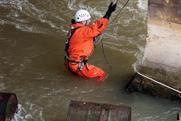 Man in protective gear and wearing a harness being lowered into rushing waters
