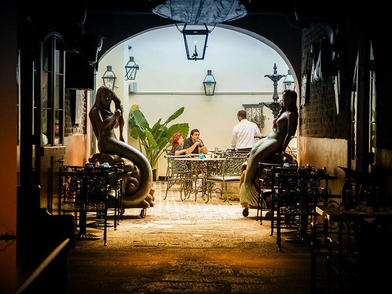 Looking into a New Orleans French Quarter courtyard, two people sit at a table in the distance Looking into a New Orleans French Quarter courtyard, two people sit at a table in the distance
