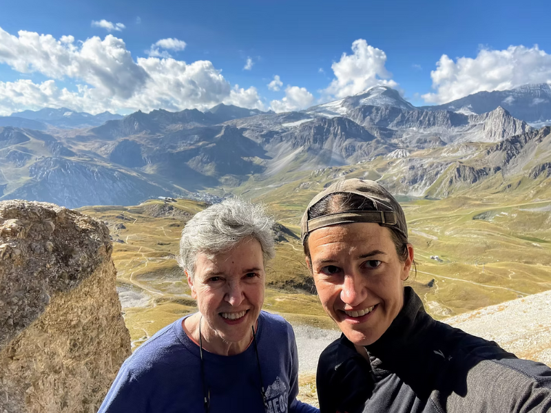 Jane Bertrand and Julie Hernandez pose on a ridge with a mountain range in the background
