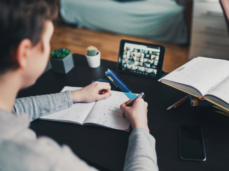 Looking over the shoulder of a student taking an online course, video screen up, notebook open.
