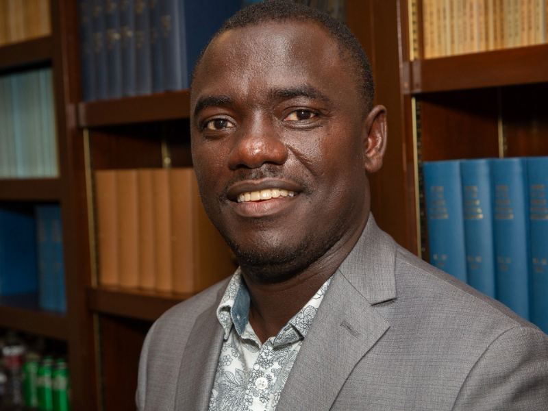 Samuel Kakraba in a grey suit jacket in front of bookshelves