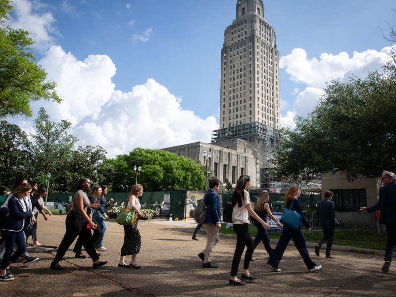 Group of public health students walking past the Capitol building in Baton Rouge under a blue sky with clouds.