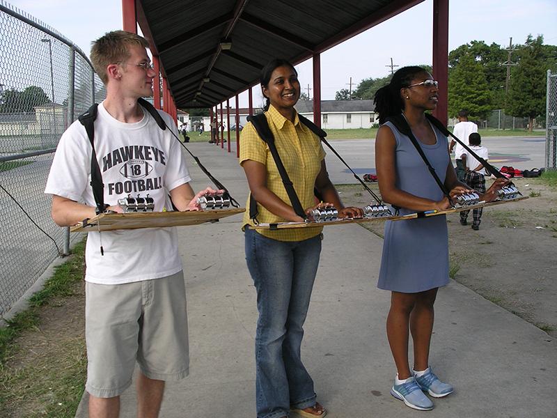 Three SPHTM students standing on school playground with serving trays
